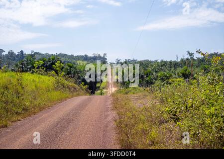 Long red dirt road winding through lush green countryside and tropical forest vegetation Stock Photo