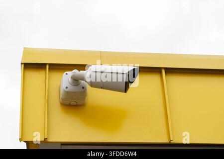 Modern surveillance camera mounted on a bright yellow exterior wall for security monitoring, safety, protection, and crime prevention Stock Photo