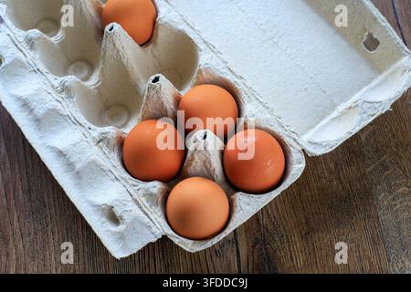 Raw brown eggs inside an open eco-friendly cardboard box on a wooden desk. Concept of wholesome diet, kitchen food storage, and fresh farm products. Stock Photo