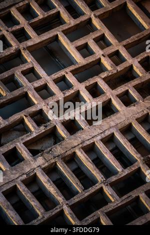 A close-up, diagonal shot shows a textured grid pattern of weathered clay bricks, forming a lattice structure with rectangular and square openings. Th Stock Photo