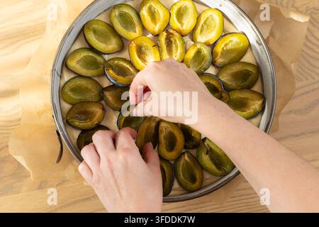 Woman hand placing fresh plum halves on raw dough in baking tin preparing plum pie Stock Photo