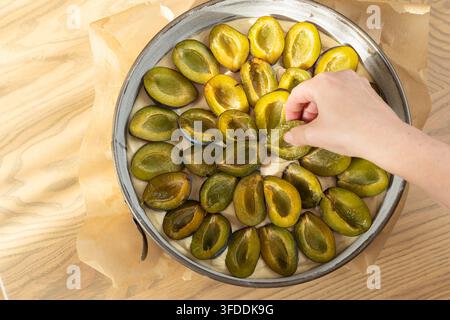 Woman hand placing fresh plum halves on raw dough in baking tin preparing plum pie Stock Photo