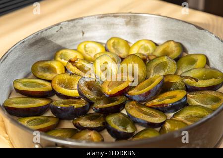 Woman hand placing fresh plum halves on raw dough in baking tin preparing plum pie Stock Photo