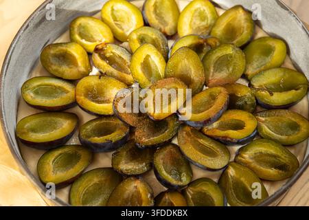 Woman hand placing fresh plum halves on raw dough in baking tin preparing plum pie Stock Photo