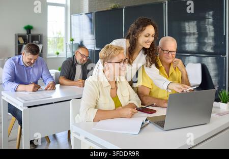 Instructor guiding senior learners on laptop in computer training classroom Stock Photo