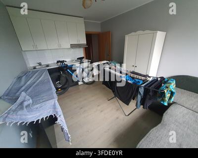 Interior view of a compact studio apartment combining kitchen and living areas. The room features light grey walls and light wood laminate flooring. Stock Photo