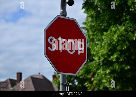 Closeup red octagonal STOP sign on metal pole, trees, rooftops and clouds Stock Photo