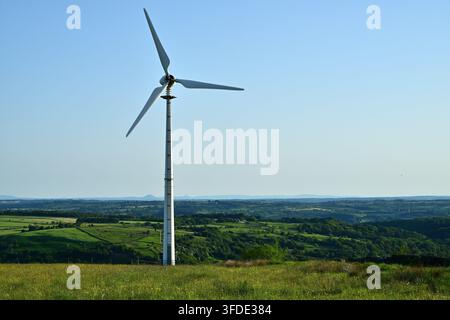Single white wind turbine on grassy hill, overlooking wide rural landscape below Stock Photo