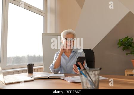 Confident middle aged senior woman euphoric winner with smartphone. Older mature lady looking at cell phone reading great news getting good result winning online bid feeling amazed. Winning gesture Stock Photo