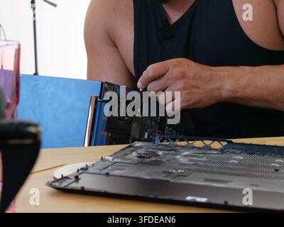 A detailed close-up shot showing a person's hands in a black tank top carefully detaching internal components from a laptop. The focus is on the intri Stock Photo