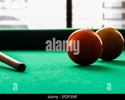 Close-up of billiard balls and pool cue on green felt table. A selective focus shot of colorful numbered balls scattered on a green snooker table with Stock Photo