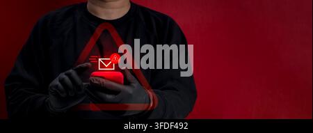 Anonymous cybercriminal scammer uses smartphone sending sms or email beneath red warning symbol and malicious message alert. Mobile phishing, credenti Stock Photo
