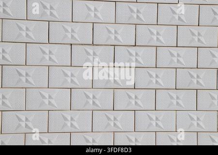 A neatly arranged white tile wall features three-dimensional cross-star embossed patterns and texture details on each tile, presenting a concise and r Stock Photo