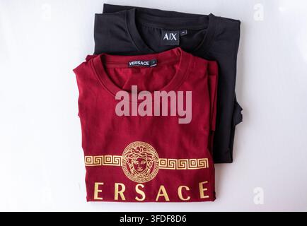 Kishoreganj, Bangladesh - 20 August, 2026 - Folded maroon Versace branded t shirt placed over black t shirt indoors. Clothing items rest on clean whit Stock Photo