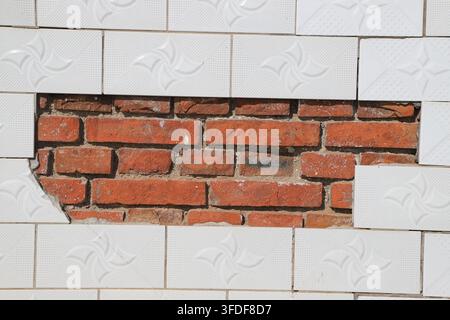 A striking contrast is formed by the white geometric patterned ceramic tile veneer and the exposed red brick wall. On one side, there is a neat modern Stock Photo