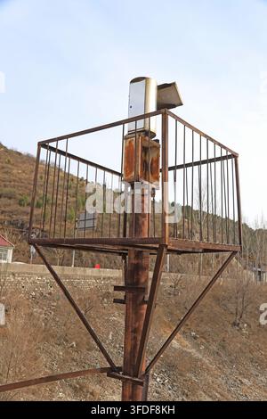 In an autumn hillside environment, a rusty metal tubular watchtower stands tall, equipped with white observation equipment on top and a square protect Stock Photo
