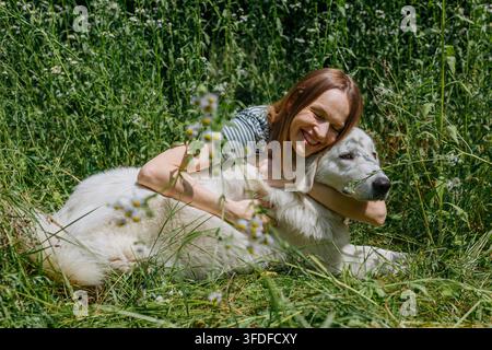 Joyful Woman Hugging a Maremma Sheepdog in a Wildflower Meadow Stock Photo