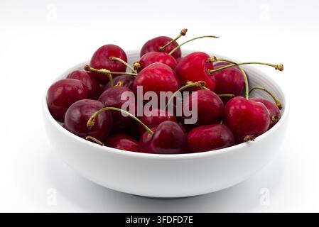 A white ceramic bowl filled with fresh ripe red sweet cherries on a white background. Stock Photo