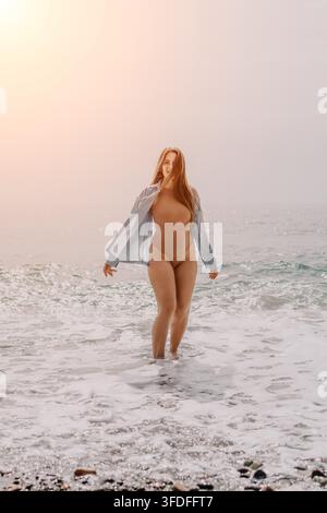 Woman beach ocean young woman stands in foaming waves wearing a bodysuit and open shirt on a misty shore with copy space Stock Photo