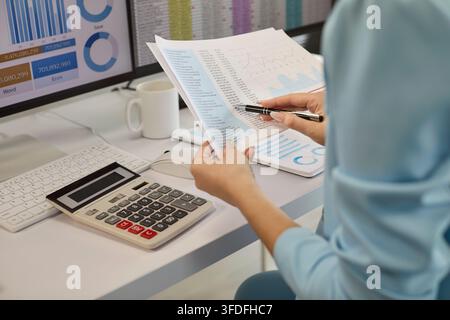 Female financial analyst checking printed data charts with pen and calculator Stock Photo