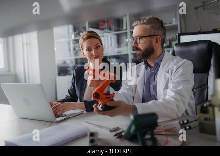 Robotics engineers working on laptop and desinging modern robotic arm in laboratory. Stock Photo