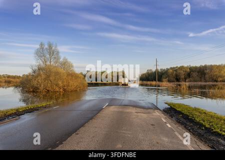A truck is driving along a flooded road. Natural disaster, spring flood. A road in a rural area is flooded with water. Spring river flood. Stock Photo