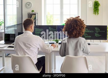 Developers pair programming at multi monitor workstation in modern bright office Stock Photo