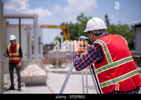 Construction surveyors wearing safety helmets and reflective vests working on site using theodolite Stock Photo