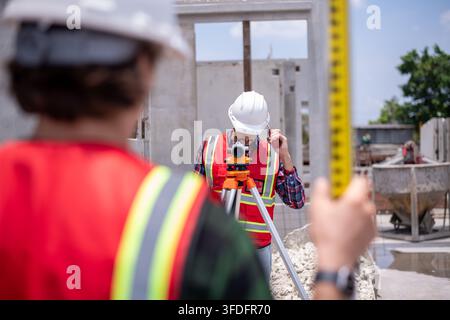 Construction surveyors wearing safety helmets and reflective vests working on site using theodolite Stock Photo