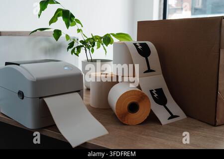 Label printer, paper rolls and fragile shipping labels for small business order fulfillment. Packaging automation streamlines ecommerce operations and Stock Photo