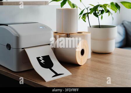 Packaging printer with rolls of labels and fragile shipping symbol for small business fulfillment. Packaging automation streamlines order processing Stock Photo