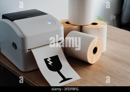 Packaging printer with rolls of labels and fragile shipping symbol for small business fulfillment. Packaging automation streamlines order processing Stock Photo