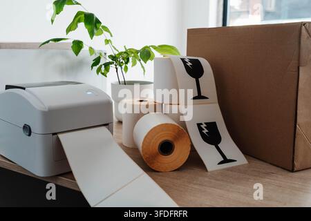 Label printer, paper rolls and fragile shipping labels for small business order fulfillment. Packaging automation streamlines ecommerce operations and Stock Photo