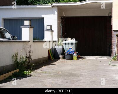 Sunny exterior shot of a residential driveway and garage area. Shows clean white boundary walls with square post lights, dark garage doors, and variou Stock Photo