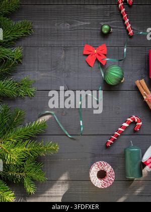 Festive Christmas flat lay featuring colorful baubles candy canes ribbon ornaments cinnamon sticks and evergreen branches arranged on a dark wooden ba Stock Photo
