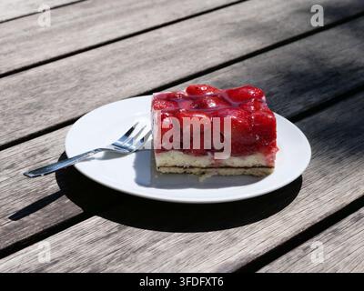 Clear close-up of a square slice of strawberry cake featuring fresh red strawberries set in clear glaze on a light sponge base. Served on a white plat Stock Photo