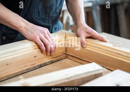 Carpenter assembling wooden parts of vintage window frame at workbench in restoration workshop. Stock Photo