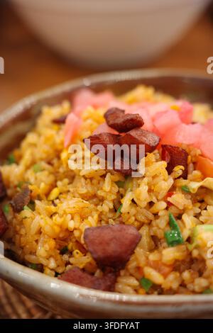 A brown earthenware pot holds golden Cantonese-style sausage and egg fried rice. The rice is dotted with dark red sausage dices and pink pickled ginge Stock Photo