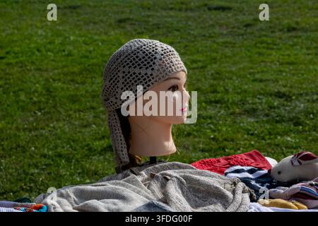 Handmade crocheted beige linen kerchief headscarf displayed on mannequin head at outdoor craft market. Traditional openwork mesh bandana bonnet featur Stock Photo