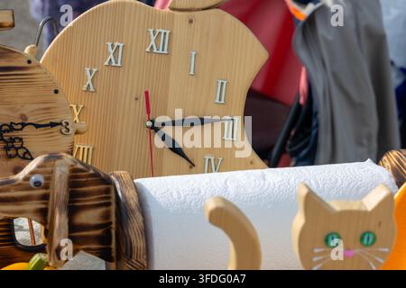 Handcrafted wooden wall clock shaped like bitten apple with Roman numerals displayed on table at outdoor craft fair. Creative artisan woodwork selecti Stock Photo
