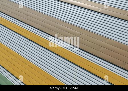 Corrugated metal siding featuring yellow, brown, and gray strips arranged in an abstract pattern, creating a modern industrial texture with strong dia Stock Photo