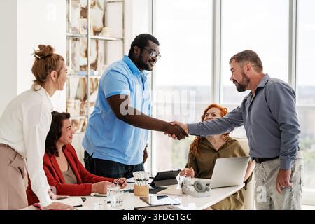 Diverse business team watches two colleagues shake hands Stock Photo