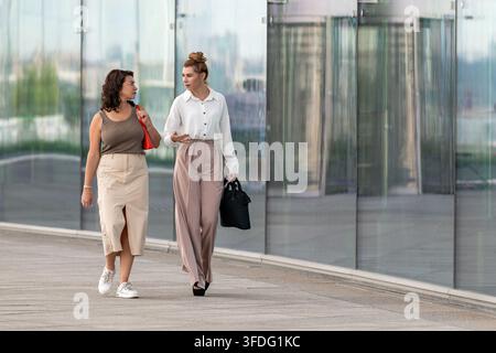 Two female colleagues walking and talking in the city Stock Photo