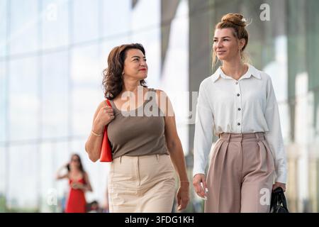 Two female colleagues are chatting on a city street. Stock Photo