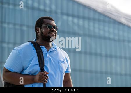 Smiling Black man with backpack walking outdoors in city Stock Photo