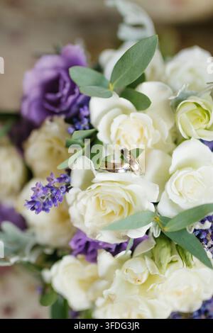 Wedding rings rest on white and purple flowers Stock Photo