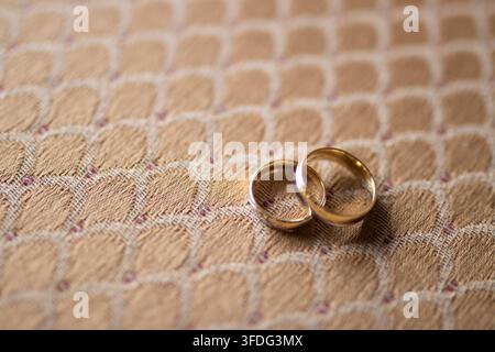Two gold wedding bands resting on patterned fabric Stock Photo