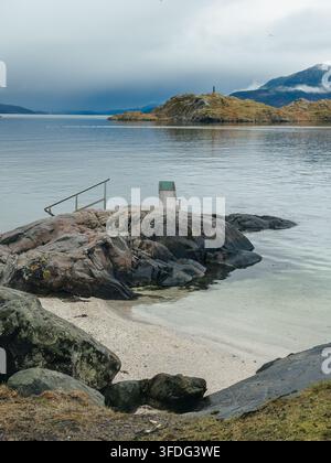 Tranquil coastal scene in Skånevik, Norway, featuring a sandy beach, calm fjord waters Stock Photo
