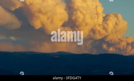 Golden smoke clouds billow over a dark mountain range Stock Photo