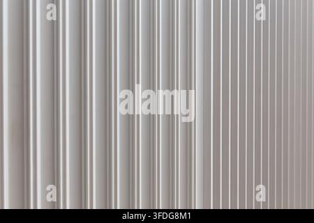 Close-up of white ribbed wall texture with vertical grooves and soft light, creating a clean minimal abstract architectural background. Stock Photo